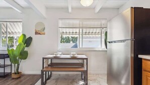 A kitchen with a stainless steel refrigerator, a wooden table with two white bowls, a potted plant, and a window with blinds.