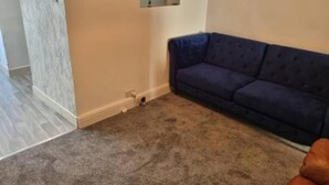 Una habitación con un sofá azul oscuro, una alfombra pequeña y un cuadro colgado en la pared.