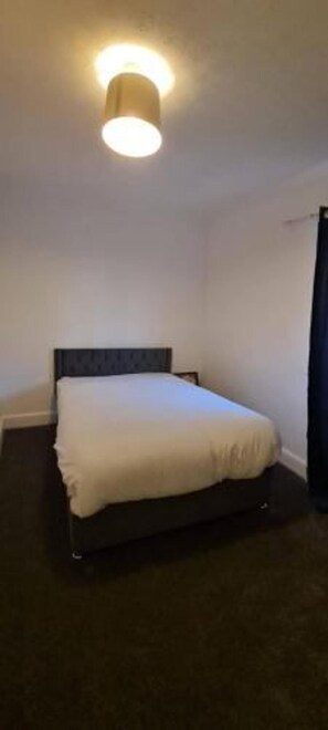 Ett hotellrum med en enkel säng, en mörk sänggavel och en taklampa.