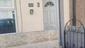 Fachada de un edificio con una puerta blanca, un ventanal pequeño y una reja de metal.