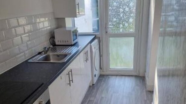 Una cocina con armarios blancos, encimera negra y ventana con vistas a zonas verdes.