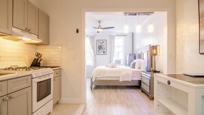 A modern kitchen with white cabinets, a stove, and a dining area with a table and chairs. - WORLD CUP + minutes to NYC (Union City)