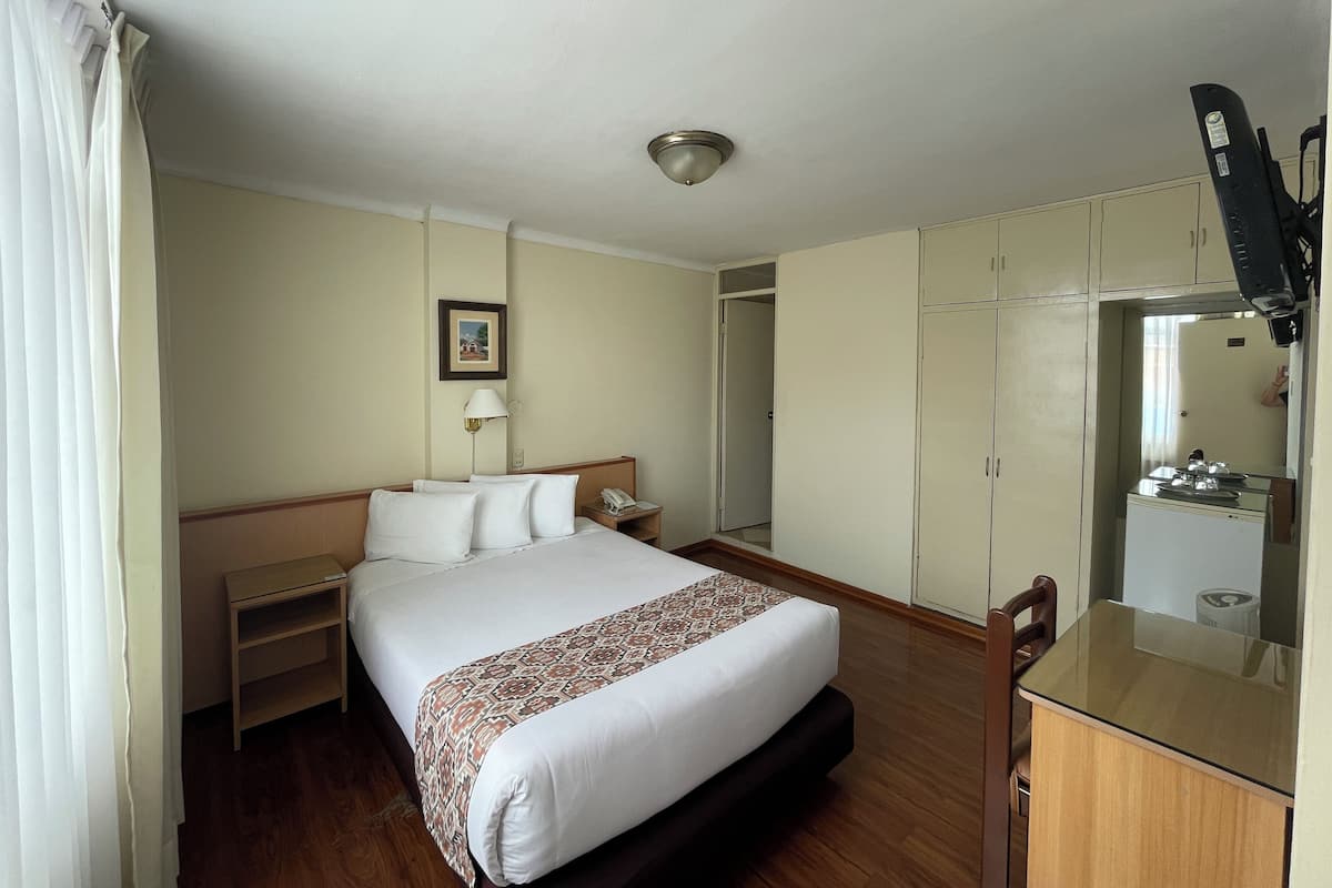 Une chambre d’hôtel comprenant un lit, une table de chevet, une lampe, une armoire et une petite kitchenette.