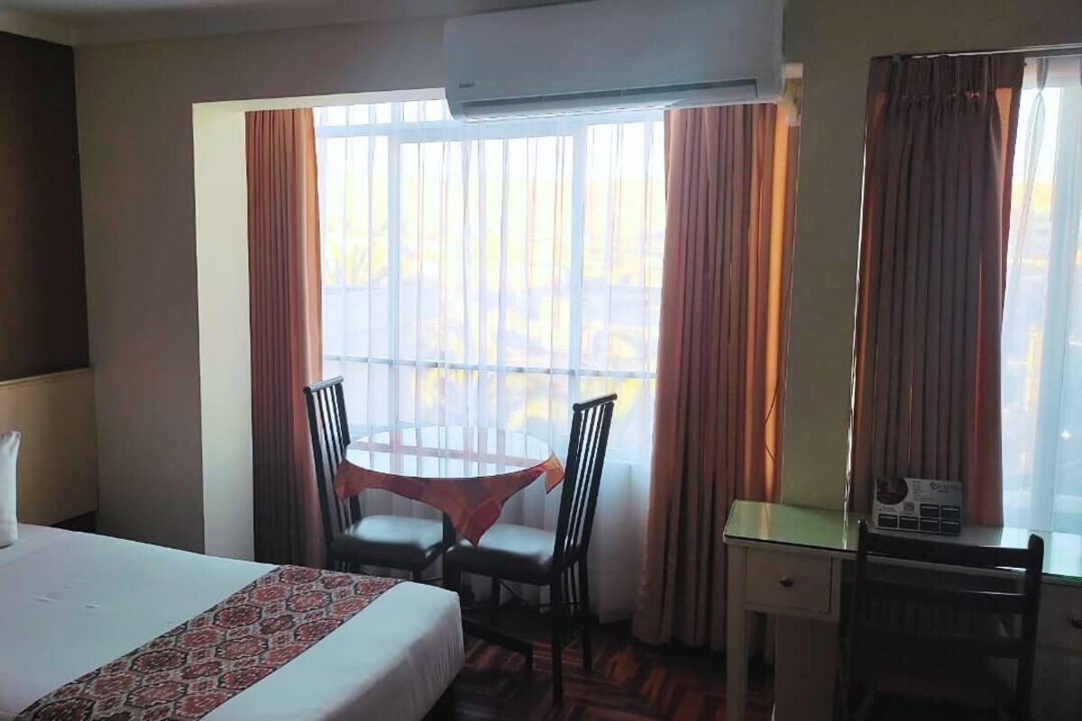 Une chambre d’hôtel avec un lit, un bureau, deux chaises et une fenêtre avec des rideaux.