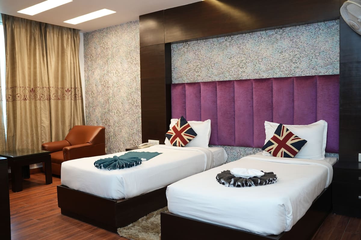A hotel room with two beds, a brown leather chair, a small table, and a large window with curtains.