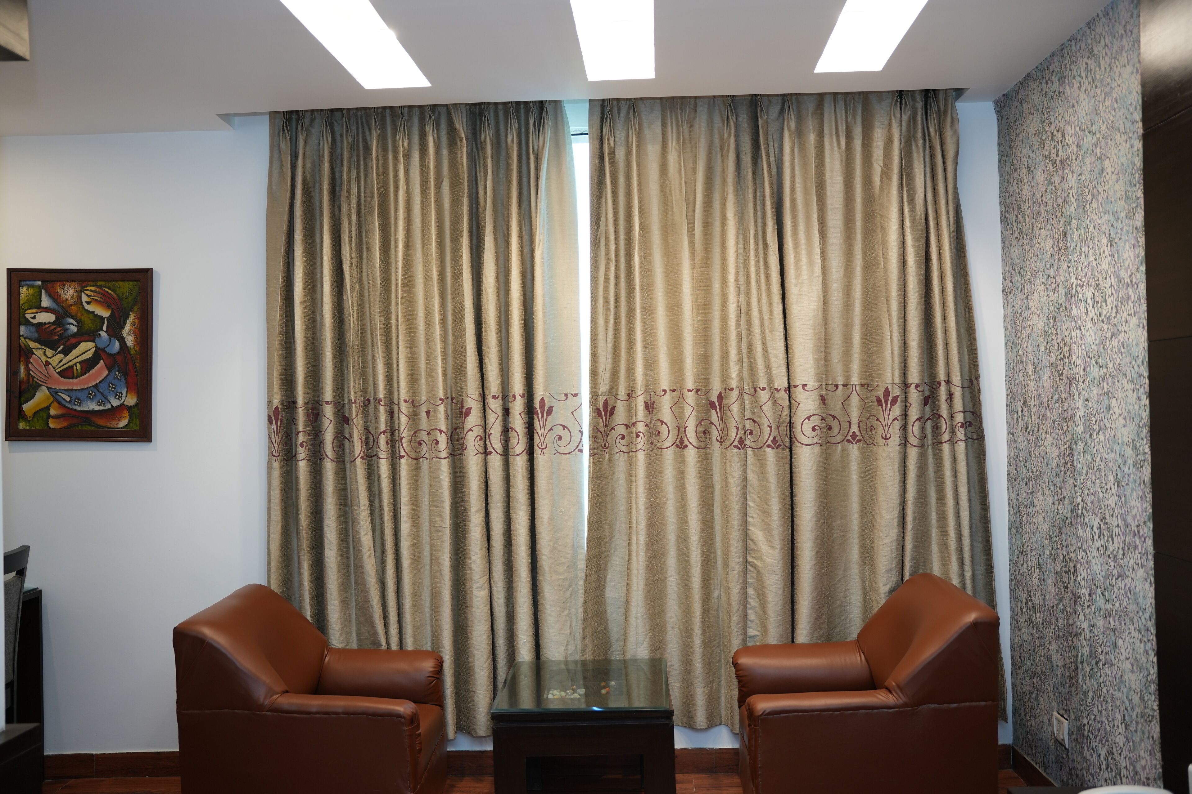 Una habitación con dos sillones de cuero, una mesa con superficie de vidrio y un ventanal con cortinas.