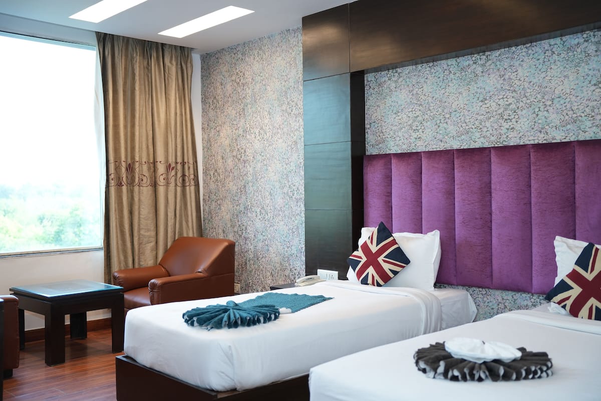A hotel room with two beds, a brown leather chair, a small table, and a window with curtains.