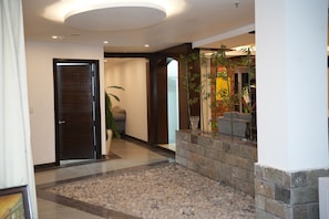 A modern lobby with a stone reception desk, a large potted plant, and a door leading to another room. - Airport Hotel Park Blue (New Delhi)