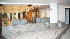 Zona de recepción con un banco de piedra, plantas de bambú en macetas y una pared de piedra.