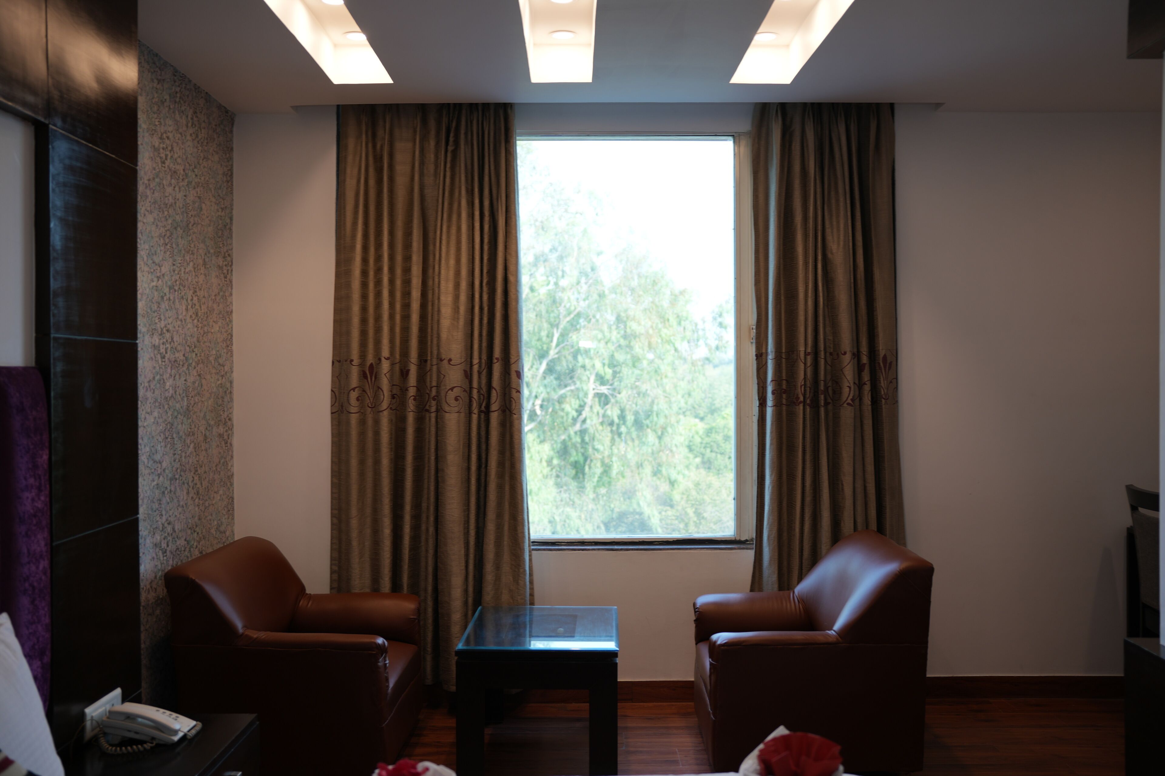 A room with two leather chairs, a small table, a telephone, and a window with curtains.