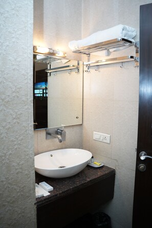 A bathroom with a white sink, a mirror, a towel rack, and a trash bin. - Airport Hotel Park Blue (New Delhi)