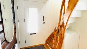 Un escalier avec des balustrades en bois menant à un palier où se trouve une porte blanche et une petite fenêtre.