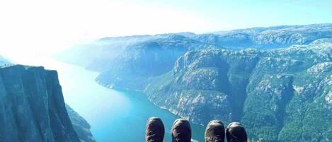 A person sitting on a cliff overlooking a deep valley with a lake.