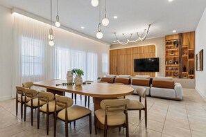 Un salon moderne comprenant un coin repas, un ensemble de canapés et un téléviseur fixé au mur.