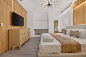 Une chambre moderne avec un grand lit, un téléviseur fixé au mur, une armoire en bois et un banc intégré.