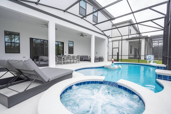 A modern indoor pool area with a hot tub, lounge chairs, and a covered seating area. - Luxury Home | BEST Resort Near Disney (6067PG) (Orlando)
