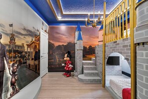 A room with a Mickey Mouse statue, a castle mural, and a bed with a white headboard.