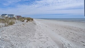 A beach with a row of houses, sandy beach, and a clear sky. - Golf Cart, Bikes, firepit, & More! (Oak Island)