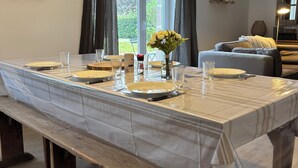 Una mesa de comedor lista con platos, vasos y un florero, con un banco al frente.