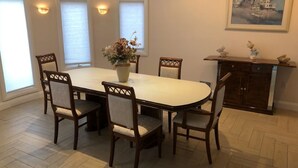 Un coin repas avec une table et des chaises, un vase contenant des fleurs séchées et un tableau accroché au mur.