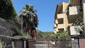 A gated entrance to a residential area with a stone wall, a palm tree, and a multi-story building with balconies.