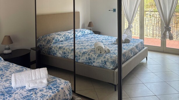A hotel room with two beds, a large mirror, a ceiling light, and a view of the outside balcony.