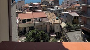 A coastal residential area with buildings, a view of the sea, and a large ship in the distance.