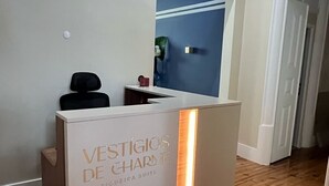 Un comptoir d’accueil avec une enseigne indiquant « VESTIGIOS DE CHARME », dans un intérieur moderne doté d’un plancher en bois et d’un mur d’accent bleu.