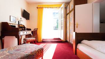 A hotel room with a bed, a desk with a piano, a chair, a television, and a large window with curtains.