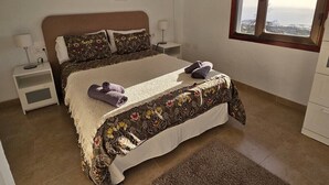 Un dormitorio con cama, mesitas de noche, ventana y una obra de arte en la pared.