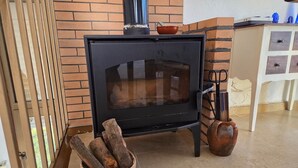 Una estufa de leña con leños en una cesta, una olla de cerámica y una pared de ladrillo.