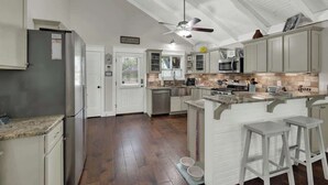 Una cocina amplia con armarios blancos, una isla central con taburetes, un ventilador de techo y un microondas integrado.