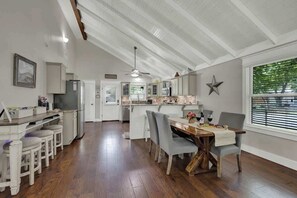 Una cocina amplia con una isla central, armarios blancos y un comedor con mesa y sillas de madera.