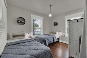 Ein Schlafzimmer mit zwei Betten, einem Fenster mit Jalousien, einem an der Wand befestigten Regal mit Dekoration und einem weißen Kleiderschrank.