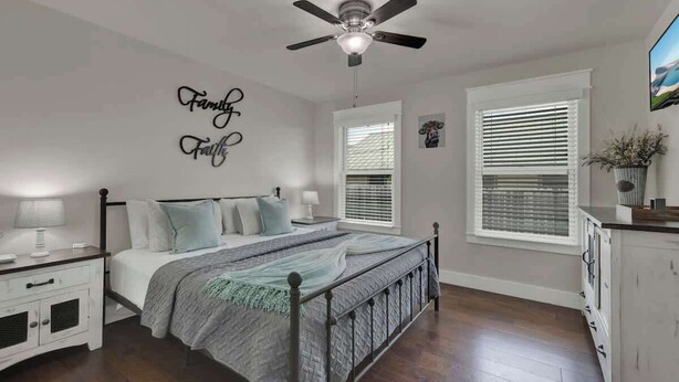 Un dormitorio con cama, mesitas de noche, ventilador de techo y un cartel en la pared que dice 'Family First'.