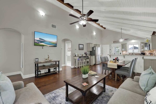 A spacious living area with a dark wooden coffee table, a television, and a ceiling fan.