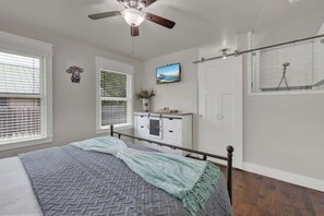 A bedroom with a bed, a ceiling fan, a window with blinds, a dresser, and a shower area.