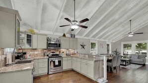 Una cocina amplia con armarios blancos, una isla central y un comedor con sofá y mesa grises.