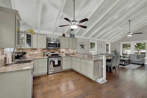A spacious kitchen with white cabinets, a central island, and a dining area with a gray sofa and table.