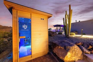A wooden sauna building with a glass door, surrounded by desert landscape and cacti. - HOZHO View House Estate (Scottsdale)