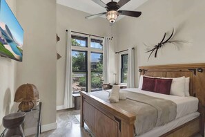 Un dormitorio con una cama grande, ventilador de techo, ventana con cortinas y un adorno de pared.
