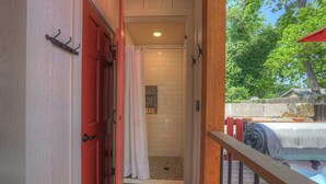 A bathroom with a shower, a towel rack, and a view of a backyard with a wooden deck and a tree. - Casa Salvia Blanca + Rojo & Tejas Combo! (Fredericksburg)