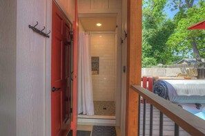 A bathroom with a shower, a towel rack, and a view of a backyard with a wooden deck and a tree.