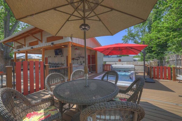 A deck with wicker furniture, a pool, and a covered area with a red umbrella.