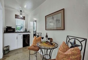 Un comedor con una mesa preparada para dos, una cocina al fondo y un cuadro en la pared.