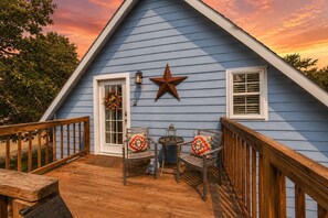 Una casa azul con un adorno de estrella, una puerta adornada con un lazo, y dos sillas con cojines sobre una terraza de madera.