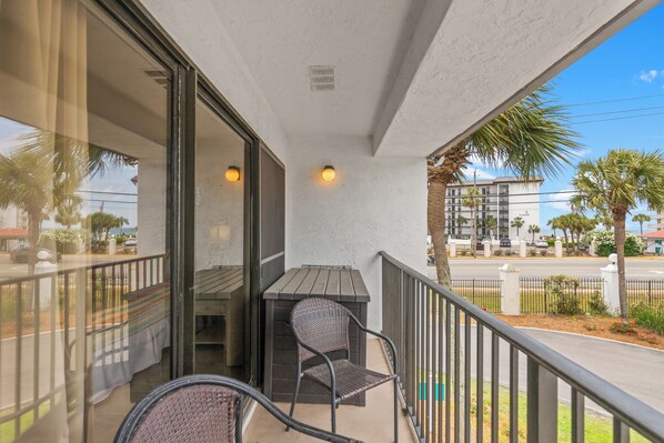 A balcony with a table and chairs, a view of the street, and palm trees.