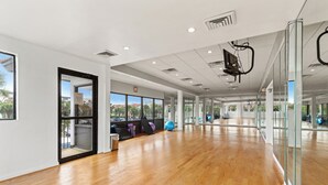 Un'ampia palestra ben illuminata con pavimento in legno, attrezzature per esercizi e ampie finestre che offrono vista sull'esterno.