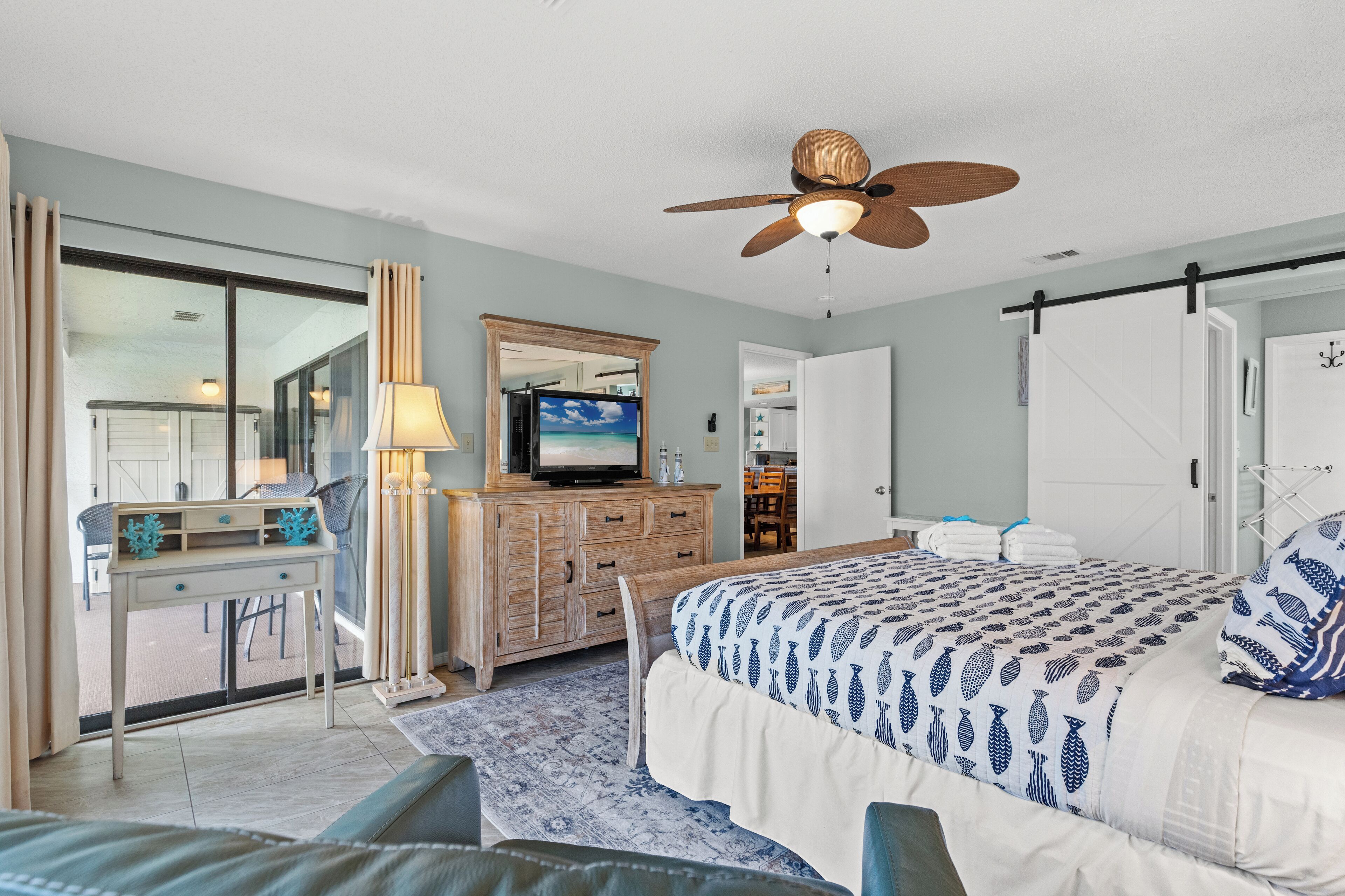 A bedroom with a bed, a desk, a dresser, a television, and a ceiling fan.