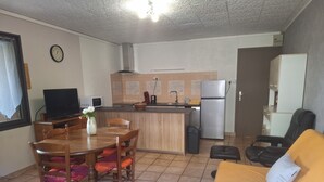 Ein kompakter Wohnbereich mit Küchenzeile, einem Esstisch mit Stühlen, einer Couch und einem Fernseher.